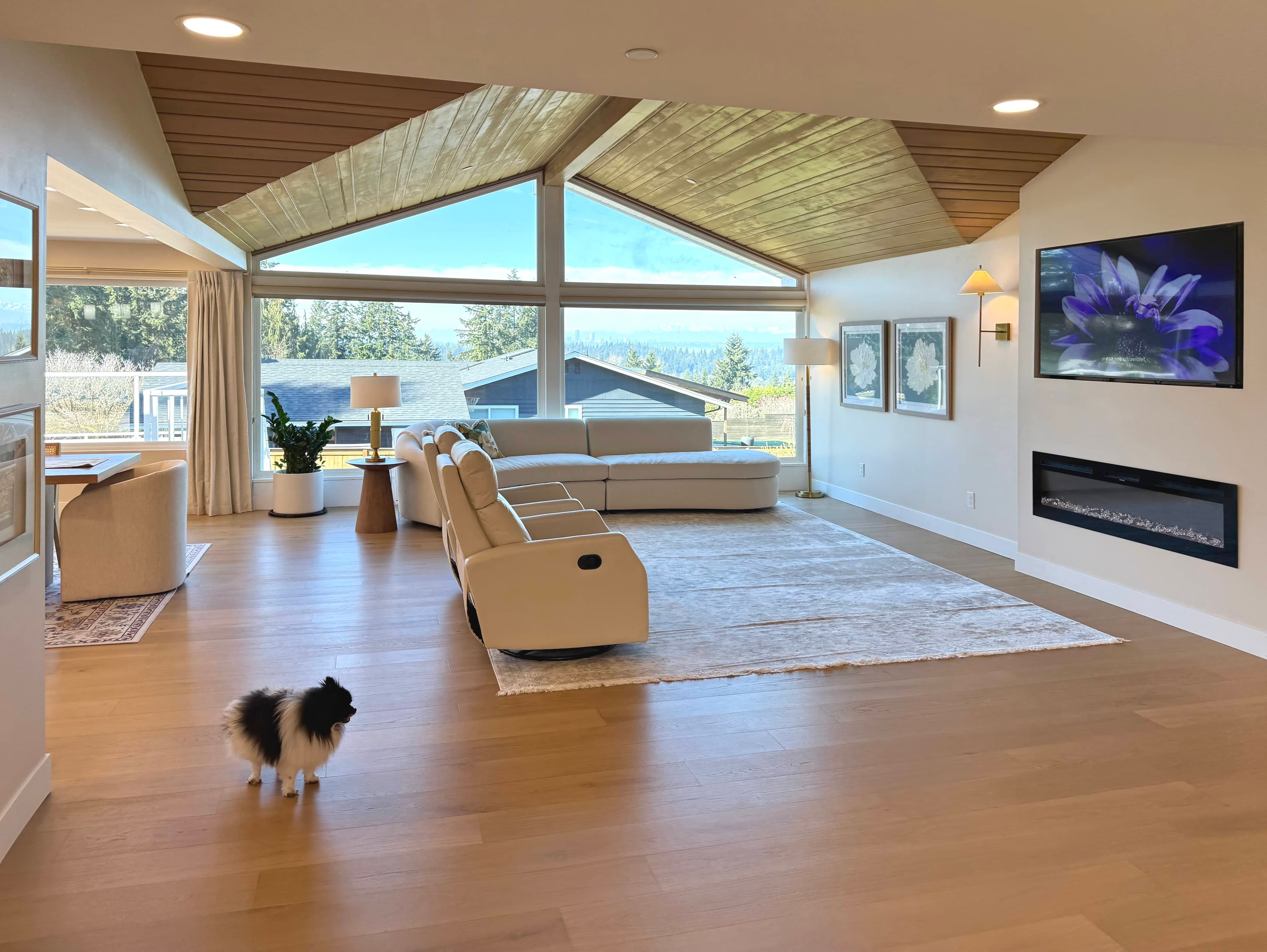 A living room at Norwood House: a vaulted wood ceiling, a cream sectional, a long fireplace, and wide windows looking out to the view.